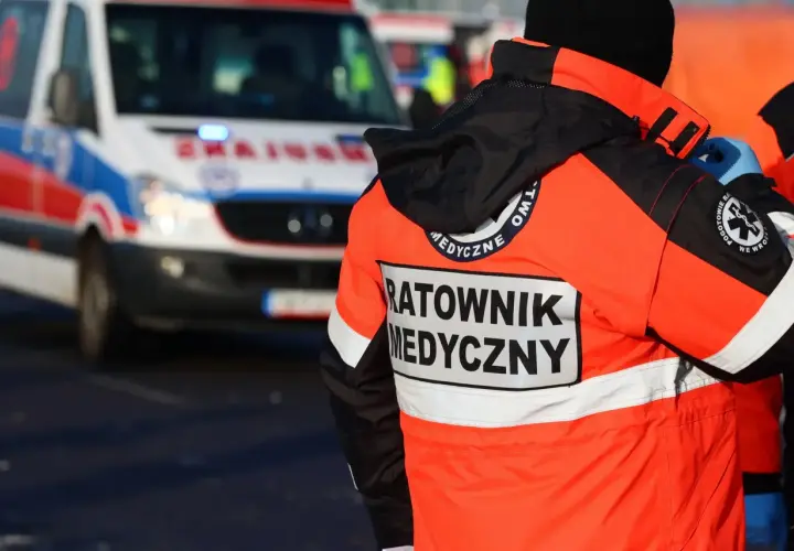 Ratownik medyczny w pomarańczowej kurtce stoi obok karetki.
