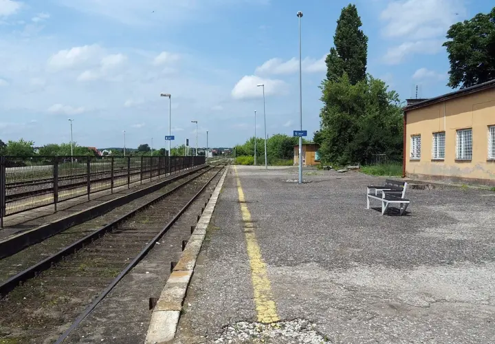 Pusta stacja kolejowa Opoczno Kielce. Torowisko, peron z ławką i żółtą linią, budynek dworca.