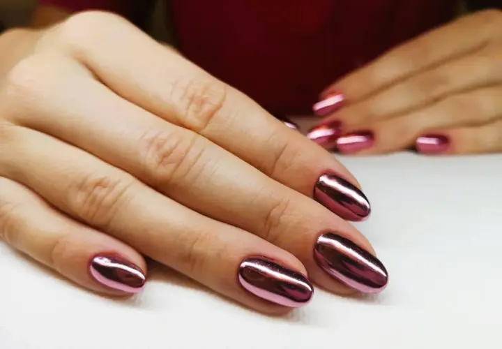 Dłonie z błyszczącym, metalicznym różowym manicure tytanowym. Czy ten efektowny manicure tytanowy rakotwórczy jest wart ryzyka?