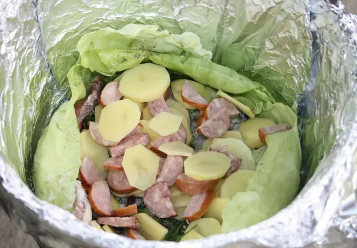 Gotowe dania na ognisko: ziemniaki, kiełbasa i kapusta zawinięte w folię aluminiową, czekają na pieczenie.