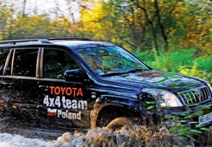 Czarny Toyota Land Cruiser 100 z napisem "4x4 team Poland" pokonuje błotnistą trasę w lesie.