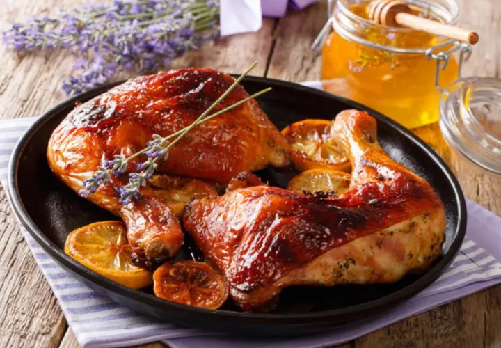 Muslos de pollo al horno dorados y jugosos, servidos con rodajas de limón y un toque de lavanda. Un tarro de miel dorada acompaña este delicioso plato.
