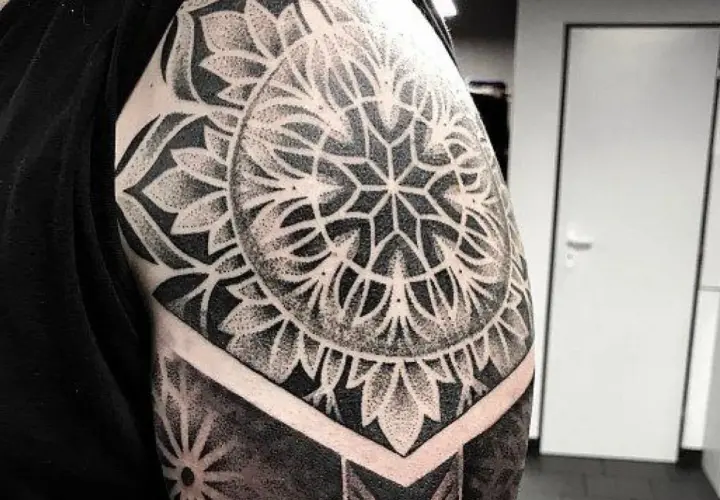 Elegancki tatuaż mandala damski na ramieniu, wykonany techniką dotwork. Wzór przypomina kwiat lub słońce.