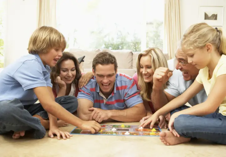 Familie spielt ein kooperatives Brettspiel, lachend und konzentriert auf dem Boden liegend.