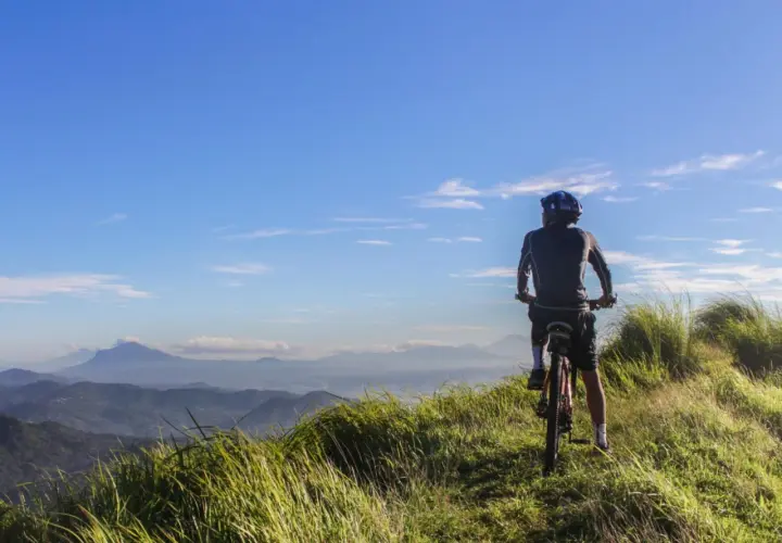 Ciclista en la cima de una colina, disfrutando de las vistas de Galicia en bici. El cielo azul y las montañas de fondo crean un paisaje impresionante.