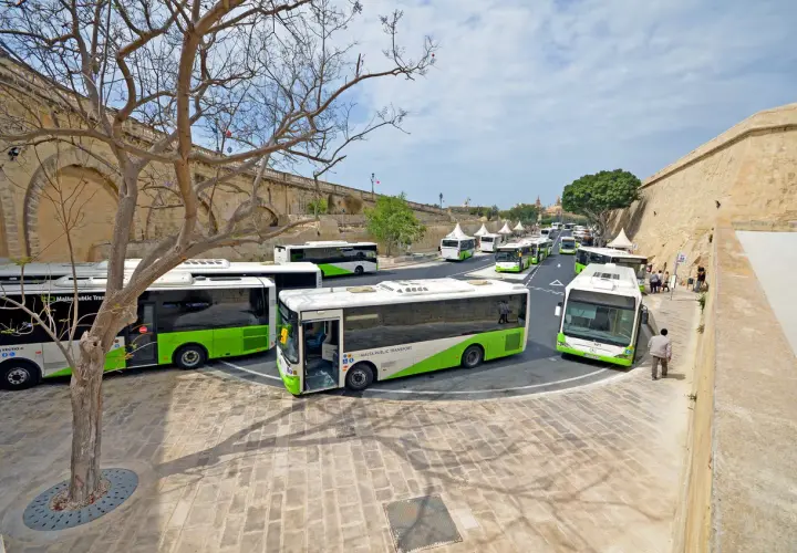 Autobusy Malta Public Transport czekają na pasażerów. Wiele zielono-białych pojazdów ustawionych w rzędzie, gotowych do odjazdu z okolic lotniska.