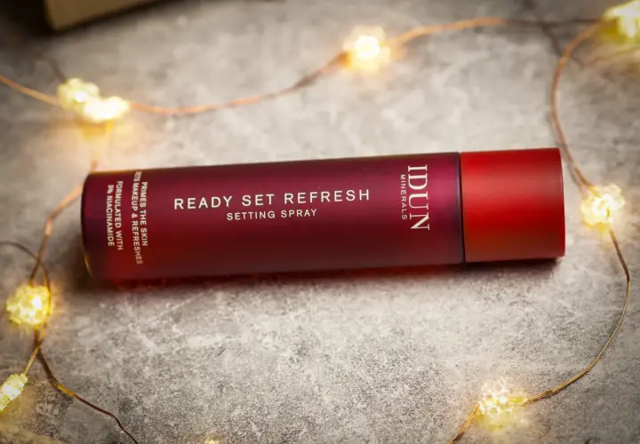 En röd flaska med IDUN Minerals Ready Set Refresh Setting Spray ligger bland julbelysning.