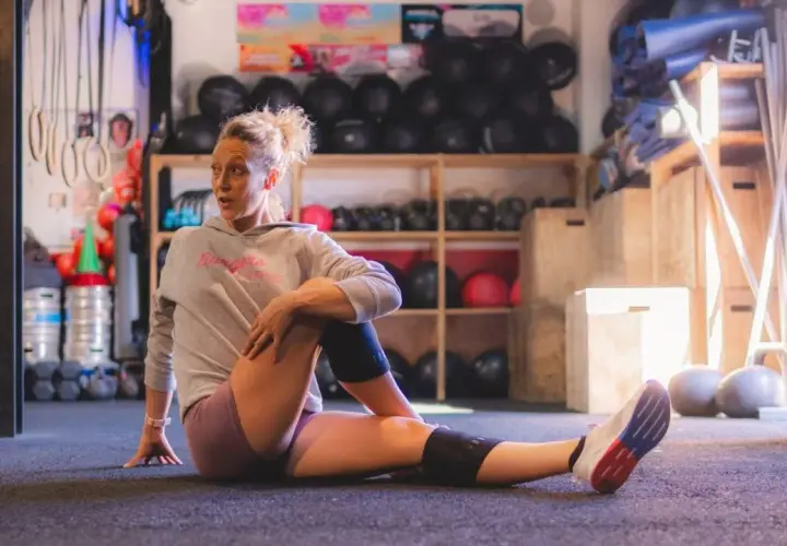 Femme en tenue de sport s'étirant au sol, profitant des bienfaits des étirements dans une salle de sport.