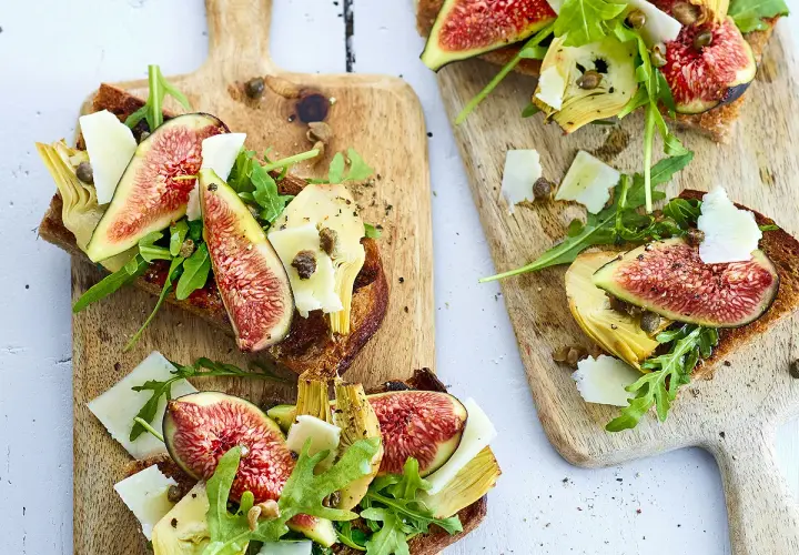 Tartines de pain grillé garnies de figues fraîches, d'artichauts, de roquette et de copeaux de parmesan.