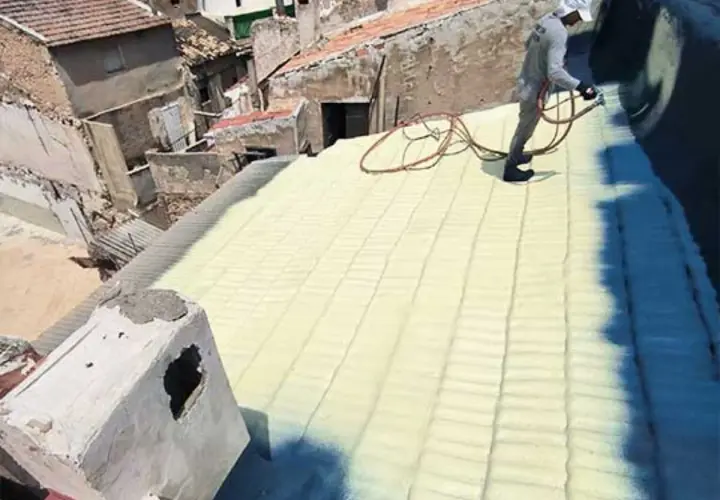 Trabajador aplica aislamiento con poliuretano en un tejado. La espuma amarilla cubre las tejas, creando una capa protectora.
