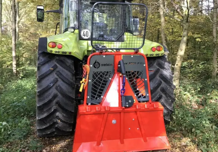 Ein grüner Traktor mit einem roten Forstkran im Wald.