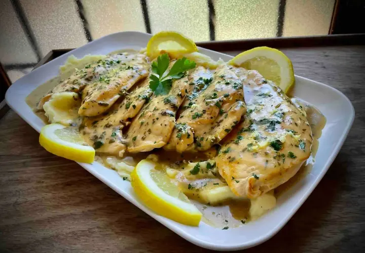 Delicioso pollo al limón con puré de patatas, adornado con rodajas de limón y perejil fresco.