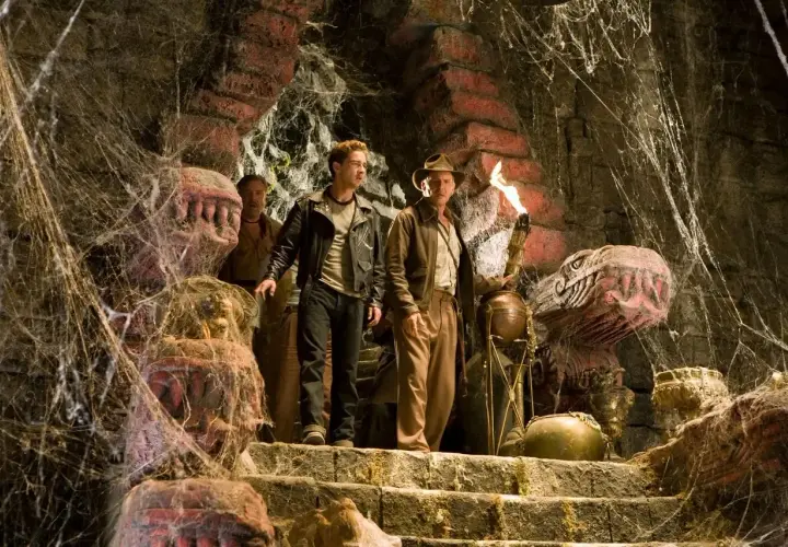 Indiana Jones i Królestwo Kryształowej Czaszki obsada: Indiana z pochodnią i Mutt na schodach w pajęczynach, obok kamiennych głów.