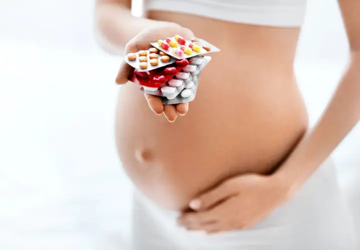 Kobieta w ciąży trzyma w dłoni opakowania leków przeciwbólowych.
