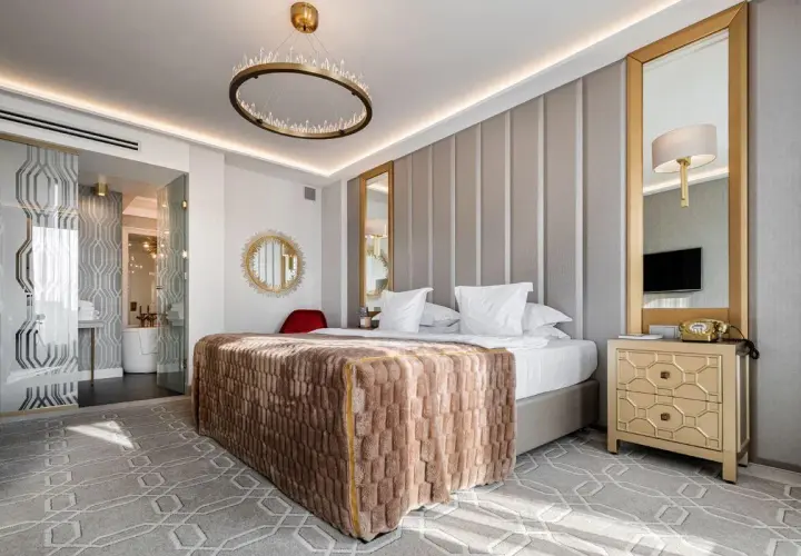 Elegancki pokój hotelowy 4-gwiazdkowy spełniający wysokie wymagania: łóżko z puszystym kocem, kryształowy żyrandol, złote lustra i stylowe meble.