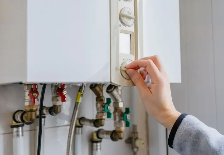 Main tenant ajuste le thermostat de sa chaudière à gaz. Une aide pour le changement de chaudière gaz est peut-être nécessaire.
