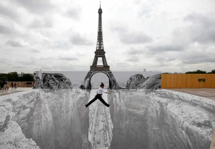Une femme saute au-dessus d'un gouffre dessiné par un peintre trompe l'oeil connu, avec la Tour Eiffel en arrière-plan.