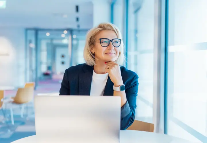 Donna bionda con occhiali, seduta al computer, pensa al suo futuro. Un nuovo capitolo, cambiare lavoro a 50 anni, è una possibilità concreta.