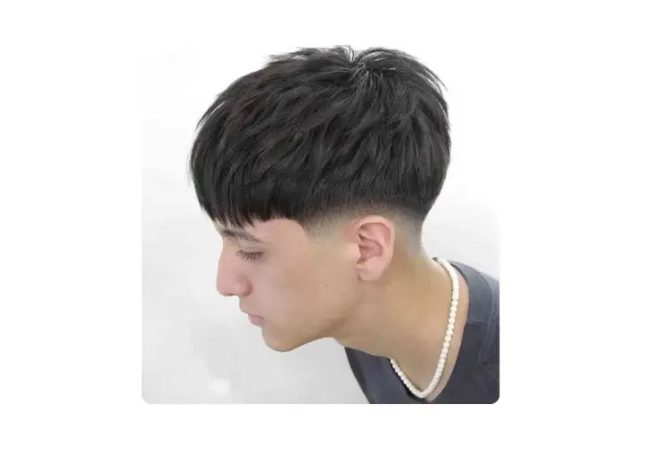 Joven con corte de pelo moderno, con flequillo recto y un degradado bajo (low fade) en los laterales.