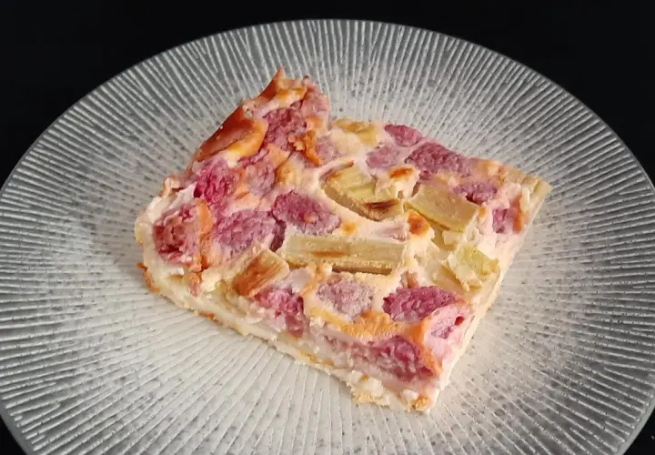 Tranche de clafoutis rhubarbe aux fruits rouges, sur une assiette transparente aux motifs rayonnants.