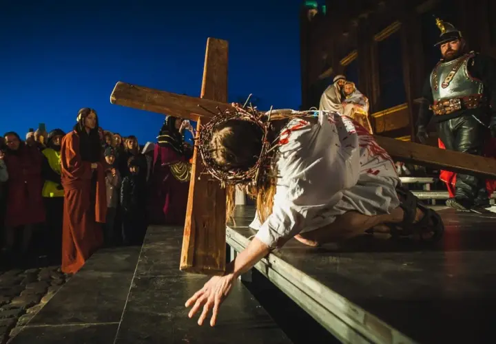 Scena kiedy jest Droga Krzyżowa: Jezus w cierniowej koronie, z krwią na szacie, upada pod ciężarem krzyża, podczas gdy tłum obserwuje.