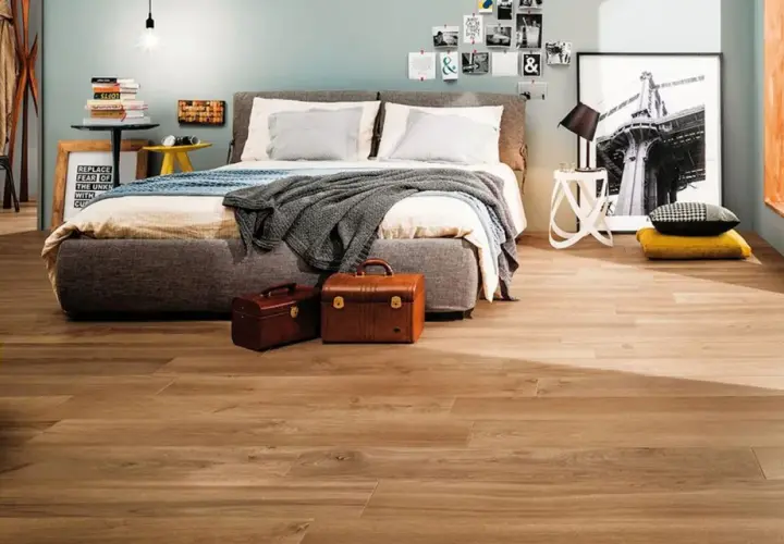Camera da letto moderna con letto grigio, poltrona gialla e pavimento in **gres porcellanato** effetto legno.