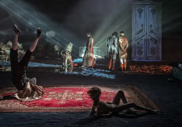 Scenograf tworzy surrealistyczny świat. Na scenie akrobata, dwie postacie w strojach z epoki i wielkie drzwi.