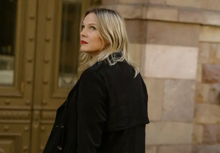 Jenny Aschenbrenner, med rött läppstift och blont hår, tittar uppåt mot en byggnad i sten.