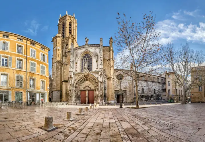 Katedra w Aix-en-Provence, z żółtą kamienicą obok, na brukowanym placu pod błękitnym niebem.