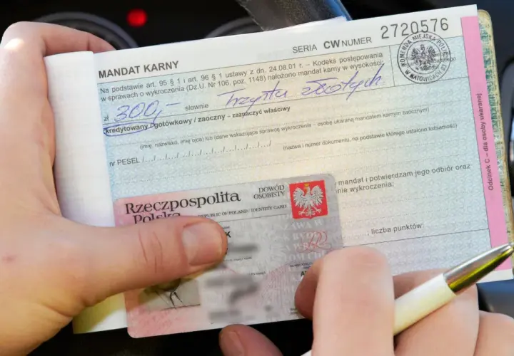 Ręka trzyma mandat karny na 300 zł za parkowanie na zakazie, obok dowód osobisty.