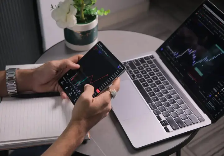 Analityk sprawdza wykresy na telefonie i laptopie, analizując dane finansowe.