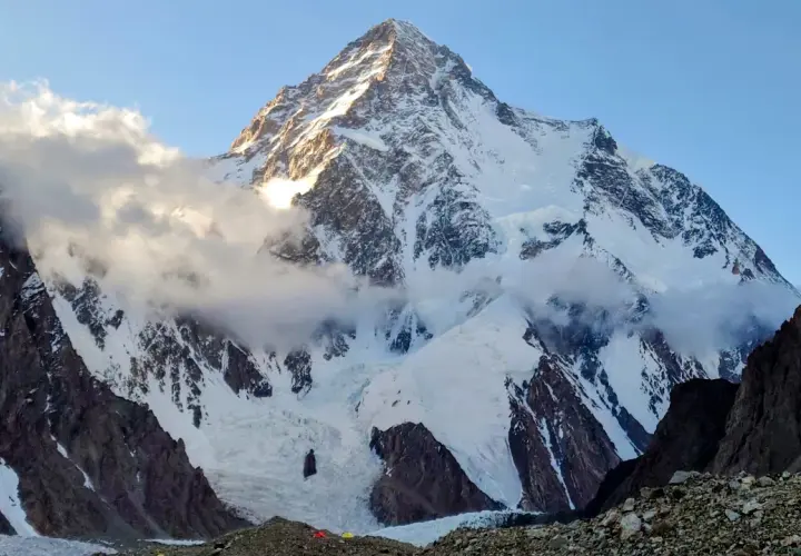 Majestatyczny K2, najwyższy szczyt Karakorum, wyłania się z chmur. Słońce oświetla jego śnieżne zbocza, ukazując surowe piękno gór.