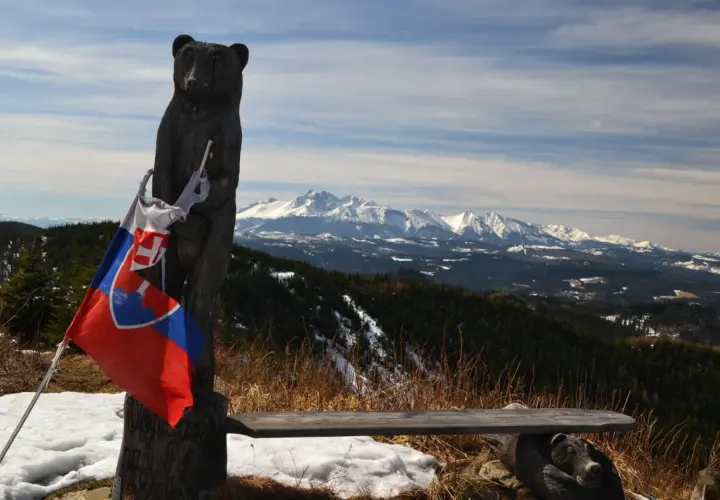 Drewniany niedźwiedź z flagą Słowacji na szczycie Veterny Vrch, z widokiem na ośnieżone Tatry.
