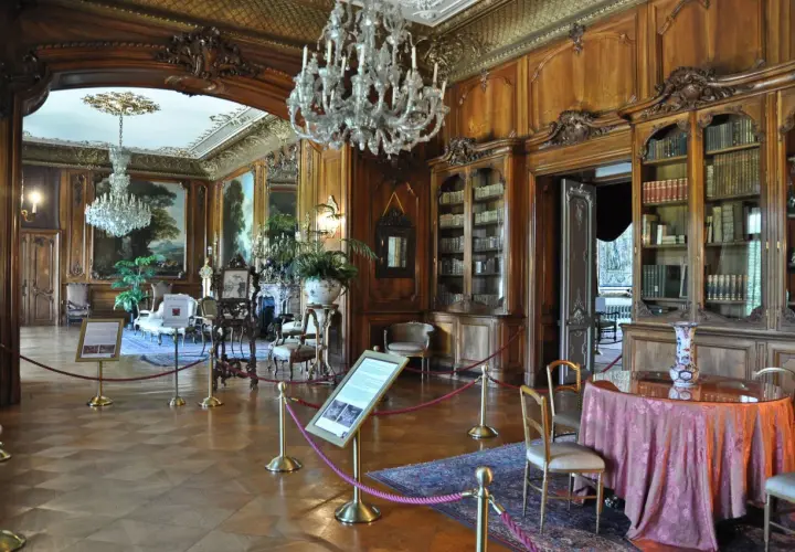 Eleganckie wnętrza Zamku w Pszczynie: kryształowe żyrandole, bogato zdobione boazerie, zabytkowe meble i biblioteka.