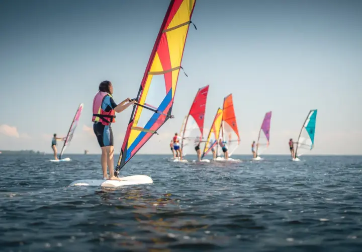 Ludzie na deskach z żaglami, uczący się, co to windsurfing. Wesoła grupa na wodzie w słoneczny dzień.