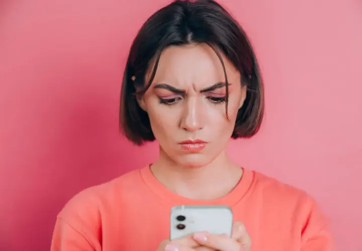 Zmarszczona kobieta patrzy na telefon, zastanawiając się, jak poprawić jakość zdjęć na Instagramie.
