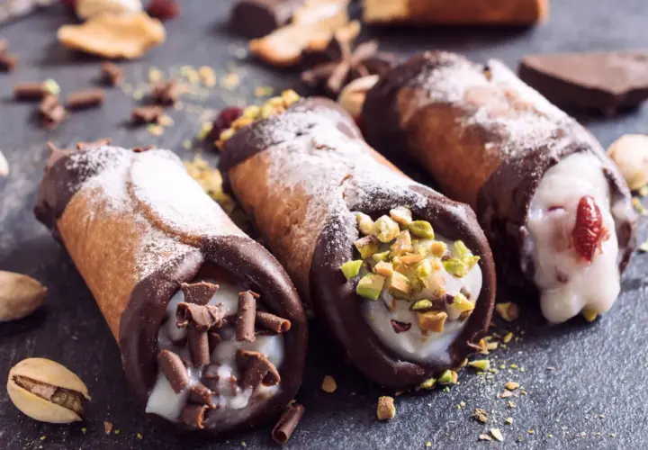 Trzy pyszne cannoli z kremem, posypane cukrem pudrem, pistacjami i czekoladą. Idealne na deser, gdy szukasz inspiracji na cannoli przepis.