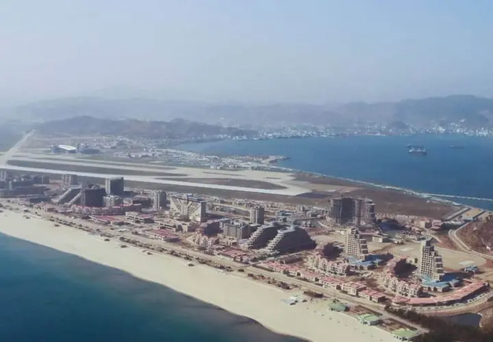 Vue aérienne d'une station balnéaire en construction en Corée du Nord, avec des bâtiments modernes, une plage et un aéroport.