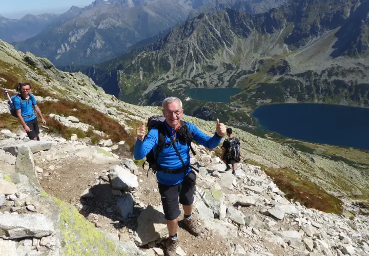 Uśmiechnięty turysta na kozi wierch trasie, z kciukiem w górze. W tle piękne Tatry i dwa jeziora.