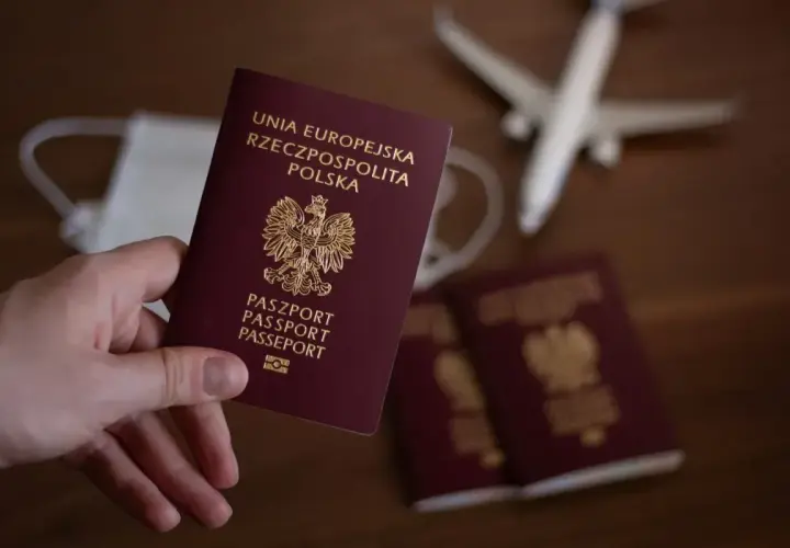 Dłoń trzyma polski paszport. Obok leżą kolejne paszporty, maseczka i samolot. Czas na podróż, ale ile wyrabia się paszport?