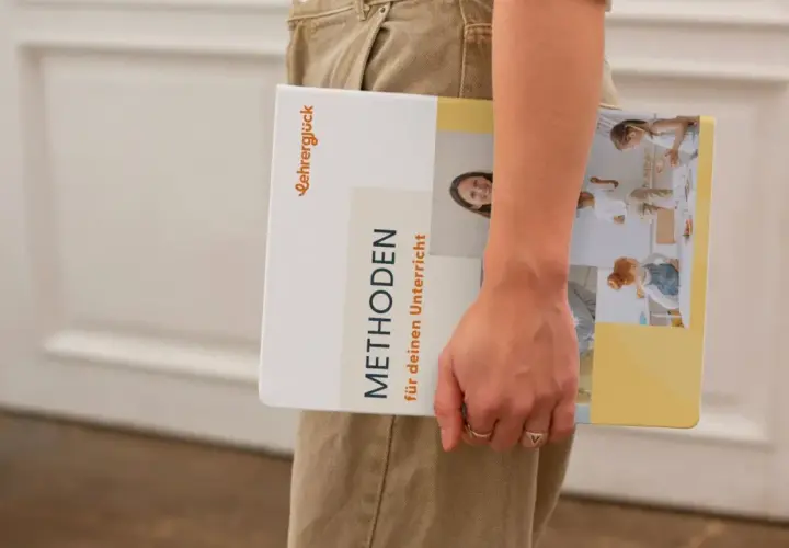 Ein Buch mit dem Titel "Methoden für deinen Unterricht" wird von einer Person gehalten. Es zeigt Bilder von Kindern in einer Lernumgebung.