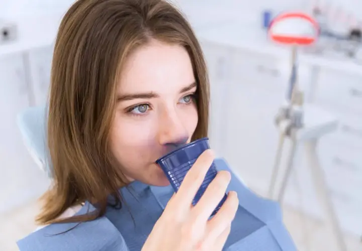 Ragazza in poltrona dentistica beve da un bicchierino blu, forse dopo un trattamento con clorexidina cos'è.