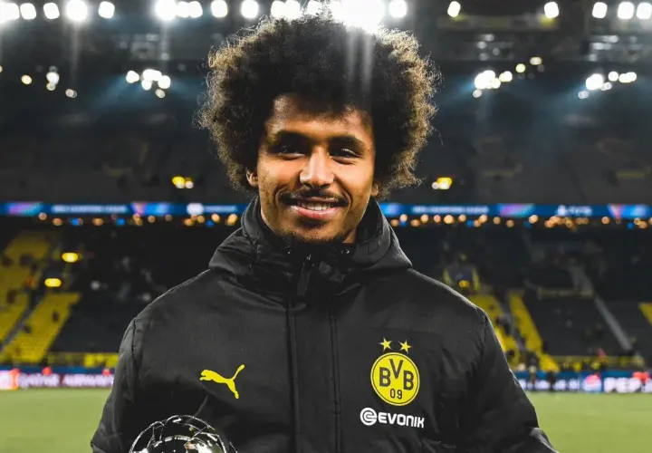 Karim Adeyemi z BVB z pucharem, uśmiecha się na tle stadionu.