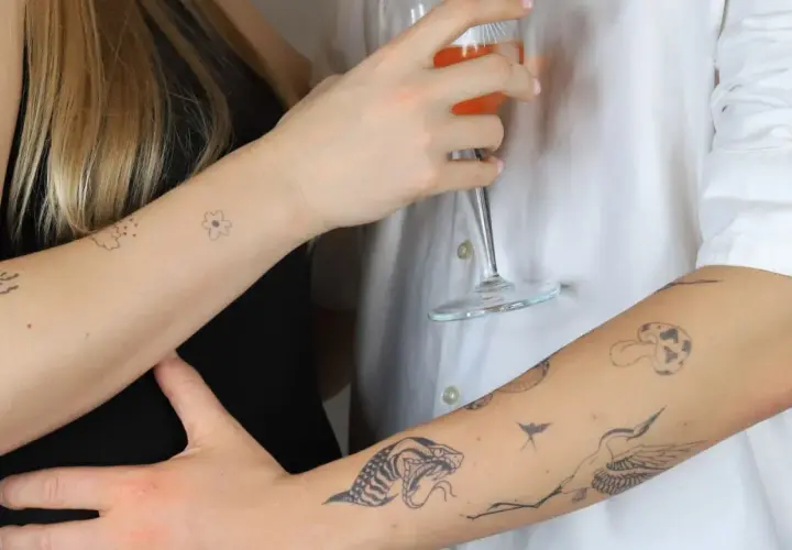 Dłonie z delikatnymi tatuażami: serce, kwiat, oko, wąż, żuraw. Subtelny ornament tattoo na skórze.