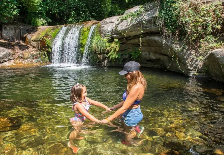 Madre e hija disfrutan de unas refrescantes piscinas naturales con una cascada al fondo.