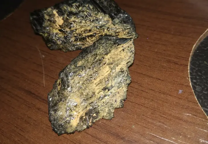 Dwa kawałki czarnego turmalinu, które pękły, pokryte żółtym nalotem, leżą na drewnianym blacie.