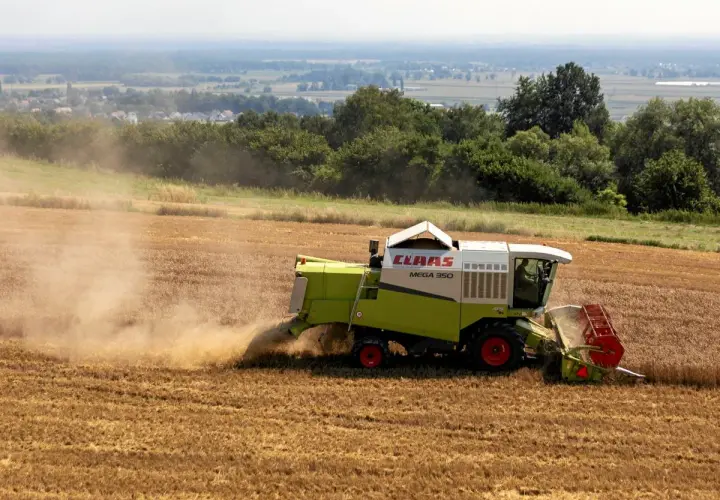 Kombajn zbożowy CLAAS Mega 350 zbiera plony na polu. Dymiące maszyny rolnicze to symbol ciężkiej pracy, która dzięki płatnościom bezpośrednim staje się bardziej opłacalna.