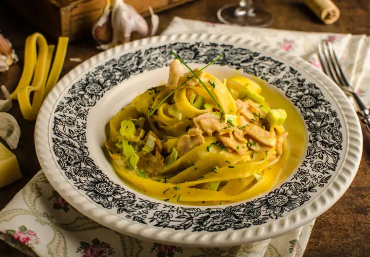 Talerz z makaronem tagliatelle w kremowym sosie z kawałkami mięsa i szczypiorkiem.