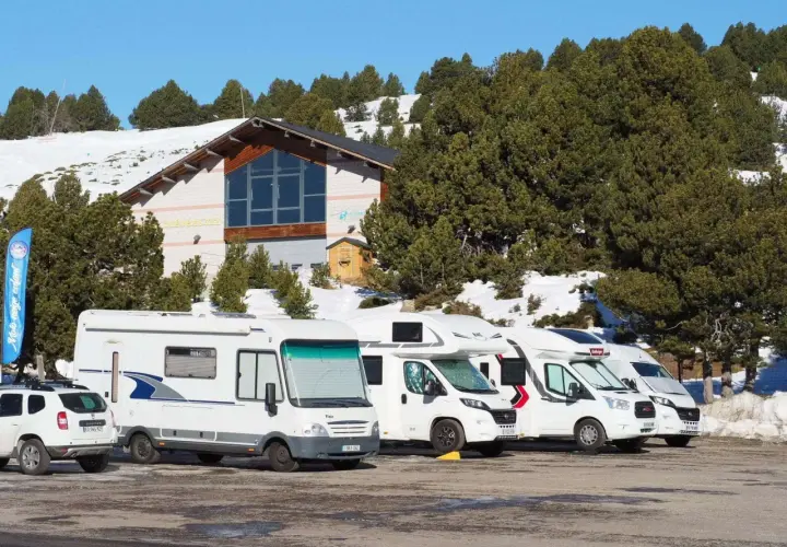 Stationnement de camping-cars dans une aire de camping car Andorre, avec un bâtiment et des pins enneigés en arrière-plan.