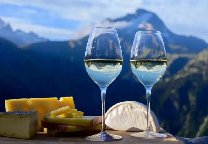 Deux verres de vin blanc avec des fromages devant des montagnes bleues.